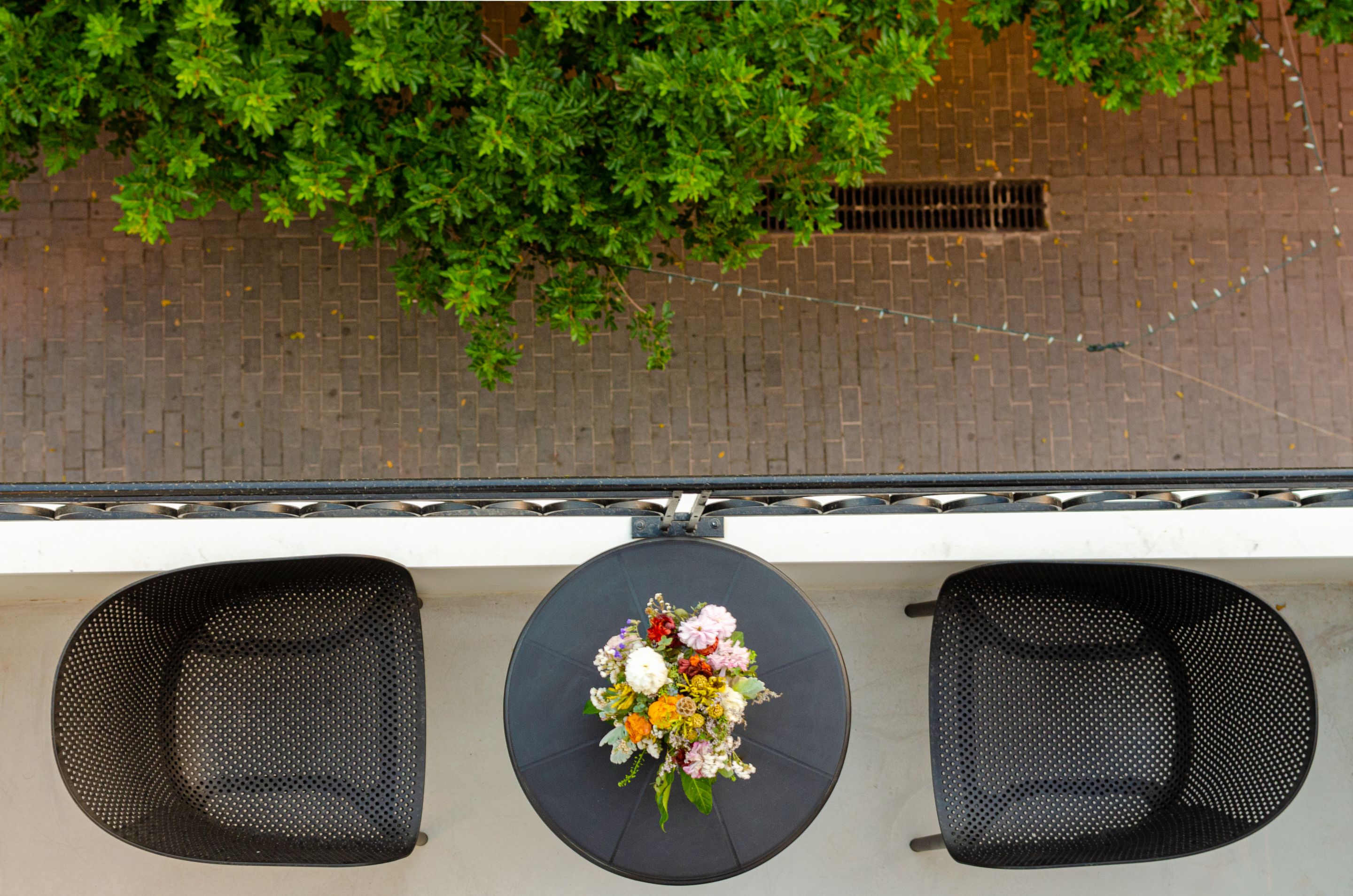 A balcony with two black chairs and a round table with a floral arrangement.