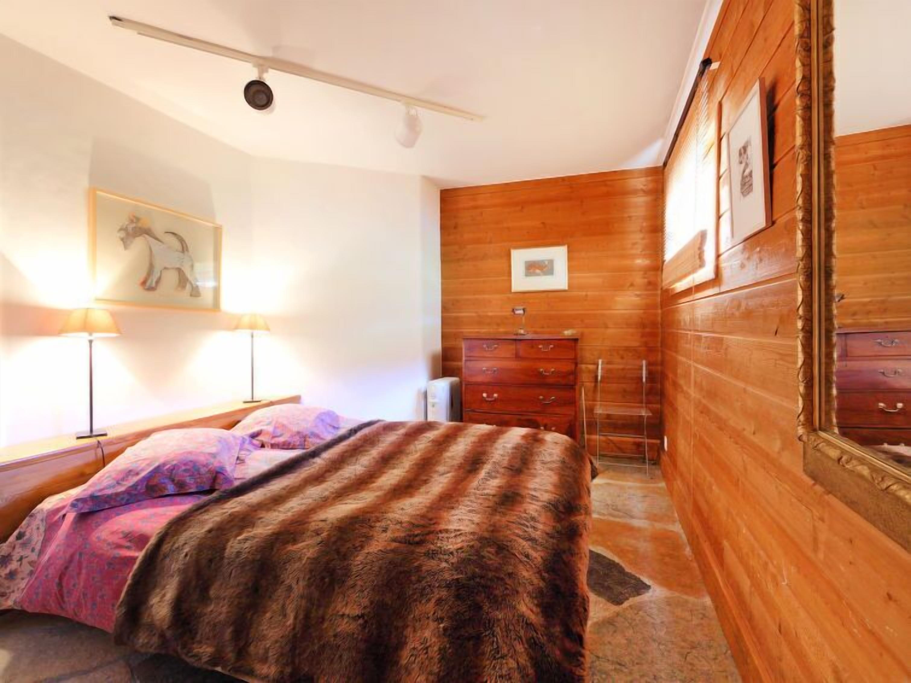 Ein Schlafzimmer mit einer Holzwand, einem Bett mit gemustertem Überwurf, einem Schmuckkästchen und einem Spiegel.
