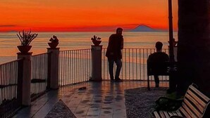 Tramonto vista da una passeggiata sul lungomare, con panchine e vasi di piante.