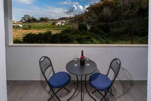 A room with a window view of a green landscape, a table with two chairs, and a bottle of wine. - Dreams Tropea Mare (Tropea)