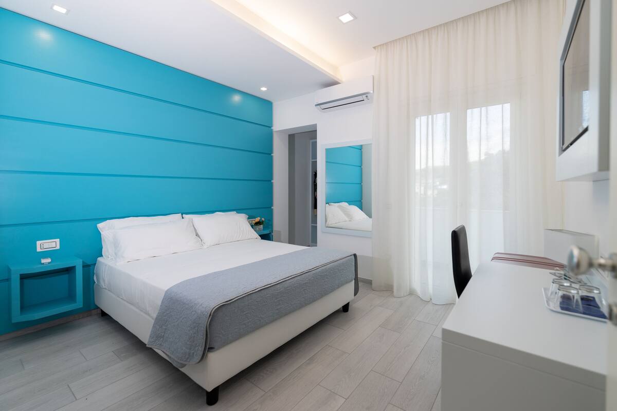 A modern hotel room with a bed, bedside table, and a desk with a chair.