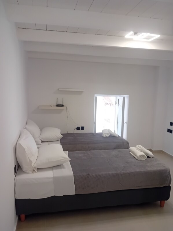 A modern bedroom with two beds, white walls, a ceiling light, and a window.