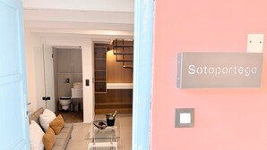 A modern interior with a glass coffee table, a sofa with cushions, a wooden staircase, and a sign reading "Sotoporrego". - Sotoportego (Χανιά)