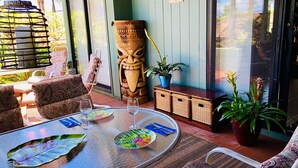 Un comedor con mesa redonda de vidrio, sillas estampadas, una escultura de máscara tiki y plantas en macetas.