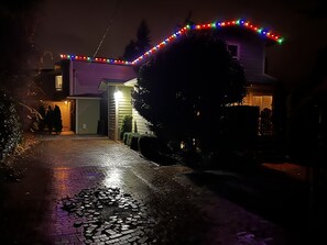 A house with a driveway leading to a garage, surrounded by trees and bushes.