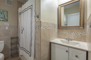 A bathroom with a shower curtain, a sink, a mirror, and a tiled backsplash.
