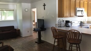 A modern kitchen with wooden cabinets, a microwave, and a coffee maker. There is a dining area with two wooden chairs and a table. - Clean and cute,1 bed, 1 bath, small town setting across from city park. (Plains)