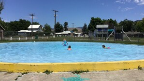 A swimming pool with a yellow safety border, surrounded by a fence, with buildings and trees in the background. - Clean and cute,1 bed, 1 bath, small town setting across from city park. (Plains)