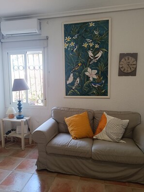 A living room with a beige sofa, a lamp, a wall clock, and a tropical bird painting. - Chalet La Costa, close to the beach and with Wifi (Chiclana de la Frontera)