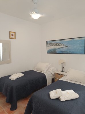 A hotel room with two beds, a painting of penguins, a ceiling fan, and a framed picture on the wall.