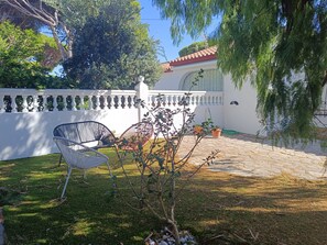 Un patio con mobiliario exterior, un árbol pequeño y una pared blanca con barandilla decorativa.