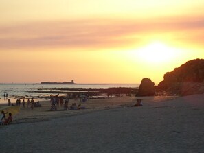 A beach with people, a rock formation, and a distant ship.