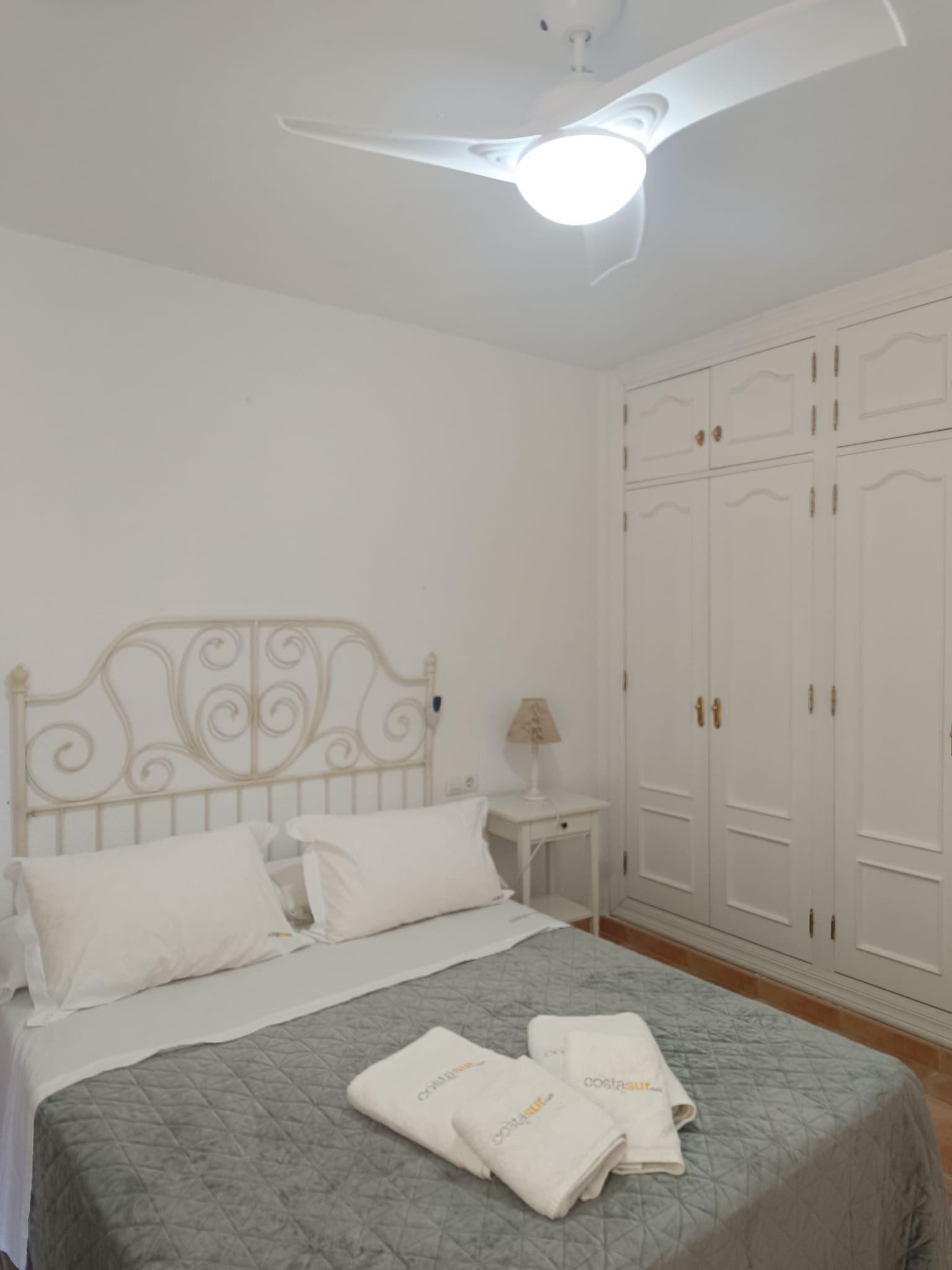 A bedroom with a bed, a nightstand, a lamp, and a wardrobe.