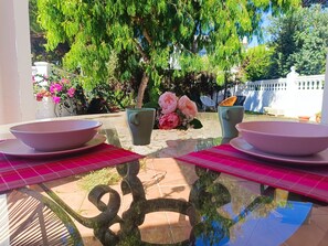 An outdoor dining area with a glass table, two bowls, and a vase of flowers.