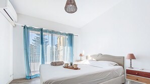 A bedroom with a large bed, a bedside table with a lamp, and a window with curtains. - Le Clos tranquille by Interhome (Nice)