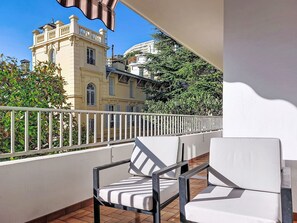 Un balcon avec des chaises blanches et une vue sur un bâtiment historique à l’architecture riche et ornée.