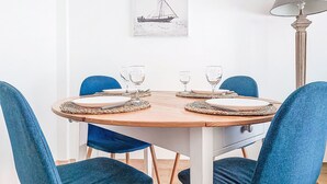 A round wooden dining table with blue chairs, set with plates and wine glasses. - Le Clos tranquille by Interhome (Nice)