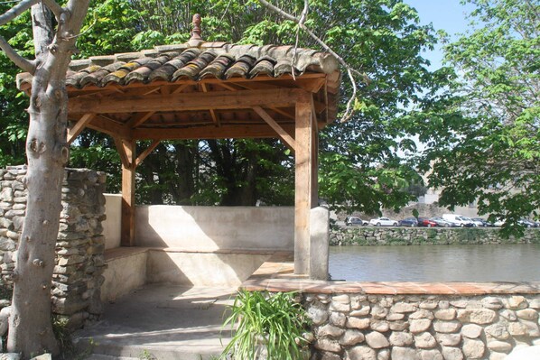 A gazebo with a tiled roof, stone walls, and steps leading to a water feature.