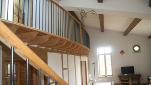 Ein geräumiger Raum mit einer Holztreppe, einem Essbereich mit Tisch und Stühlen sowie einem Fernseher auf einem Schreibtisch.