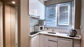 Una cocina compacta con armarios blancos, un microondas, un lavabo y una tetera.