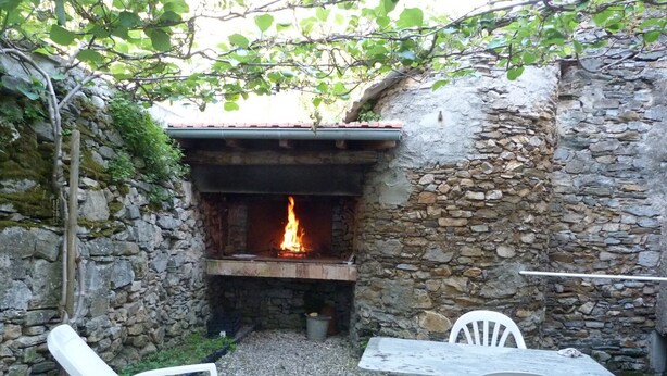 Un área de estar al aire libre con paredes de piedra, una chimenea, sillas de plástico blanco y una mesa.