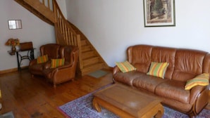 Una sala de estar con una escalera de madera, sofás de cuero y una obra de arte enmarcada en la pared.