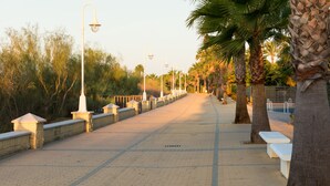 A paved walkway lined with benches and street lamps, flanked by palm trees and a stone wall. - Cozy Townhouse in Islantilla: Enjoy the Beach, Golf and Adventures (Lepe)