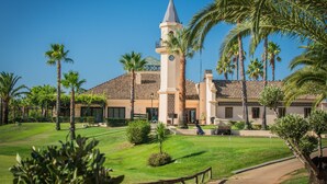A building with a tower, surrounded by palm trees and a well-maintained lawn. - Cozy Townhouse in Islantilla: Enjoy the Beach, Golf and Adventures (Lepe)