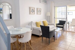 A modern living room with a sofa, two chairs, a dining table, and artwork on the wall.