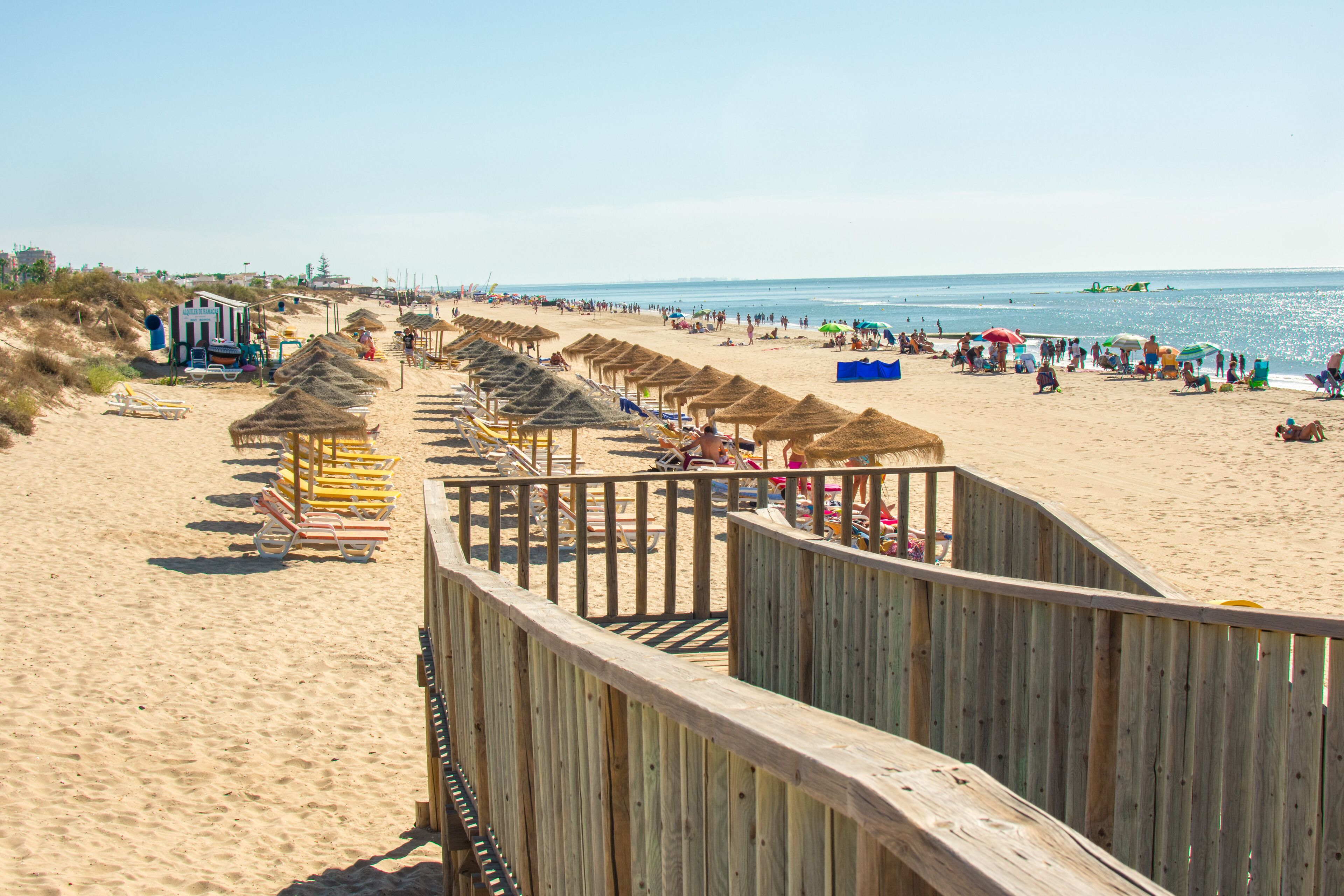 A beach with wooden walkways, beach chairs, umbrellas, and a clear view of the ocean.