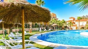 A swimming pool with white lounge chairs and a thatched umbrella. - Cozy Townhouse in Islantilla: Enjoy the Beach, Golf and Adventures (Lepe)