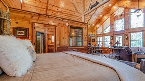 Ein Blockhaus-Innenraum mit einem großen Bett, einem Essbereich und mehreren Fenstern.