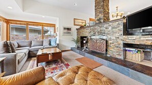 A modern living room with a stone fireplace, a sectional sofa, and a flat-screen TV. - Spacious Condo within walking distance to Chair 20 & access  to Grand Hyatt Amenities (Vail)