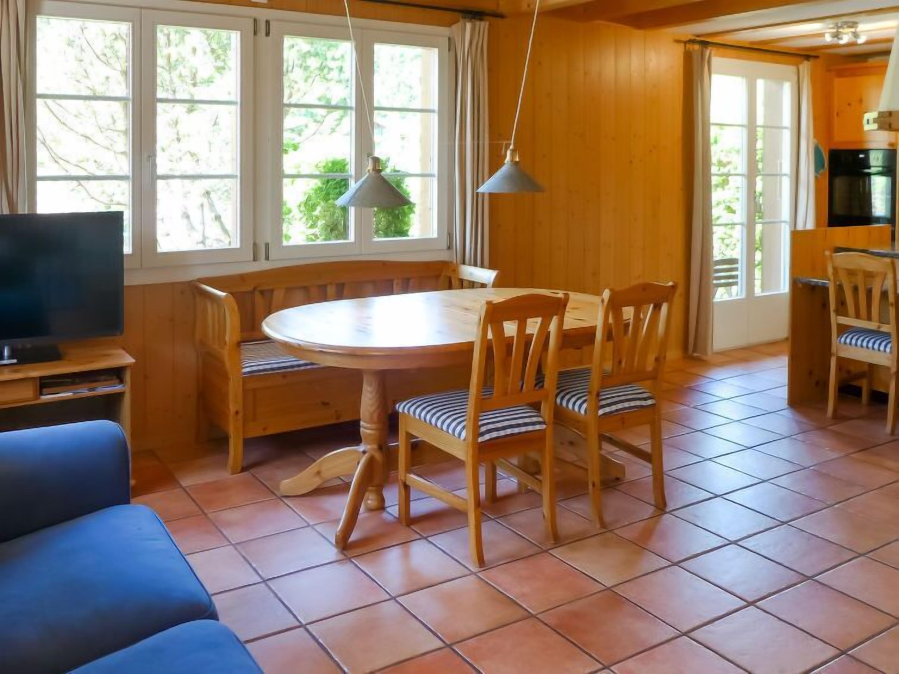 A cozy room with a round wooden table, four chairs, a blue sofa, and a television on a wooden stand.