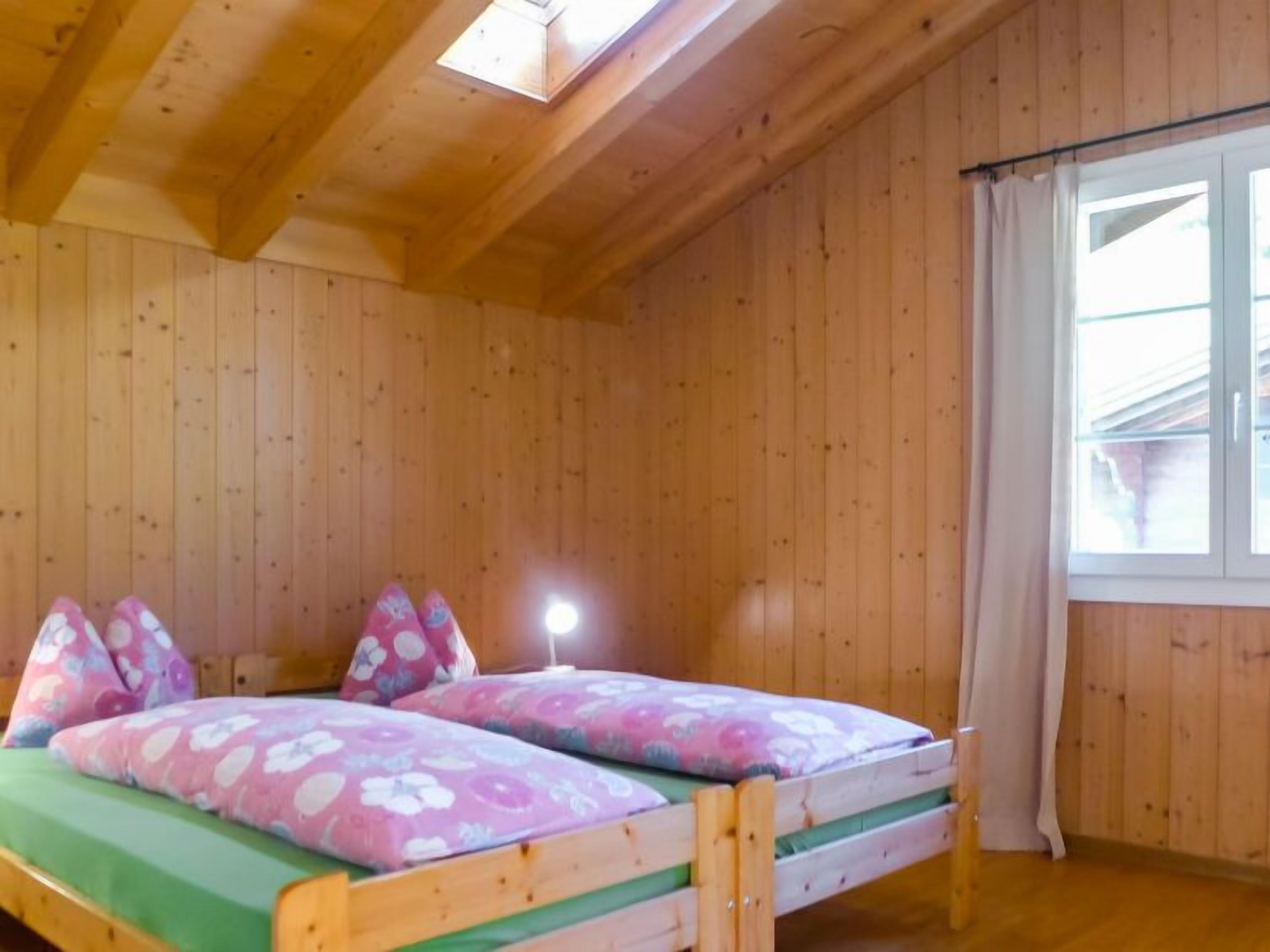 A wooden cabin room with a bunk bed, a skylight, and a window with curtains.