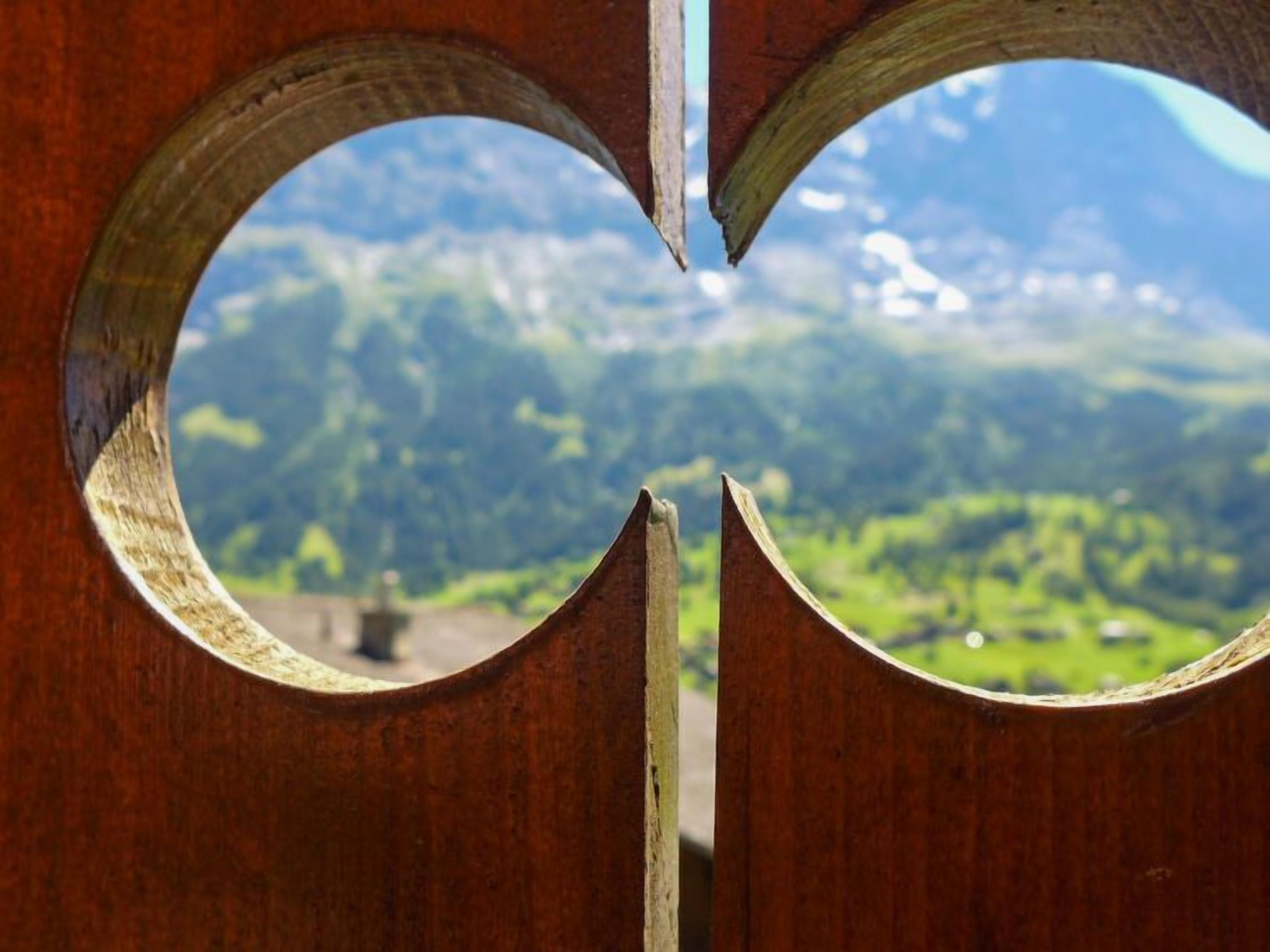Een houten constructie met ronde uitsparingen die een bergachtig landschap onthullen.