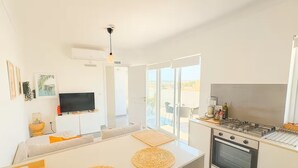 A modern kitchen with a flat-screen TV, a dining area with a white table, and a balcony with a view. - Peaceful Penthouse with large Sunny Terrace (Marsaxlokk)