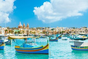 A marina with colorful boats and a historic building in the background. - Peaceful Penthouse with large Sunny Terrace (Marsaxlokk)