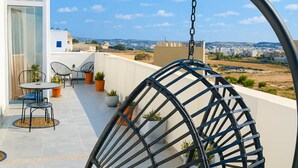 A balcony with a hanging chair, potted plants, and a table with chairs. - Peaceful Penthouse with large Sunny Terrace (Marsaxlokk)