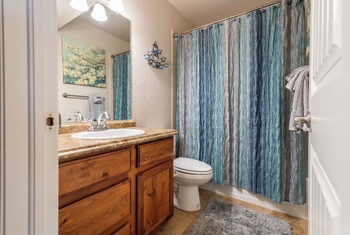 Un baño con tocador de madera, lavamanos blanco y cortina de ducha.