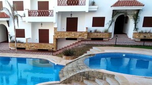 A pool area with two swimming pools, stone steps, and a building with balconies and windows. - Residence Alcazaba Oued Laou 4129 (OUED LAW)