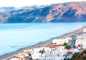 A coastal town with buildings along the waterfront, a clear view of the sea, and mountains in the background. - Residence Alcazaba Oued Laou 4133 (OUED LAW)