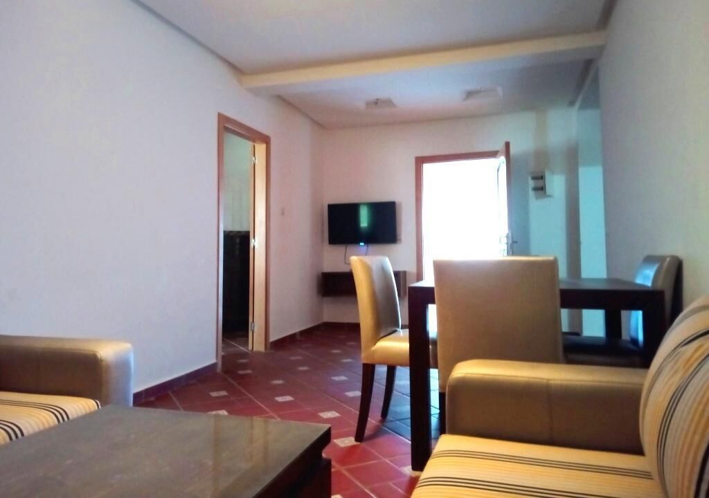Un salon comprenant un canapé, une table basse et un téléviseur fixé au mur. On y trouve également un coin repas avec des chaises et une table.