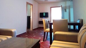 Una sala de estar con un sofá, una mesa de centro y un televisor montado en la pared. Hay un comedor con sillas y una mesa.