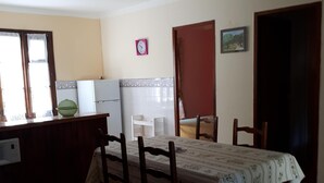Un coin repas avec une table dressée pour quatre personnes, un réfrigérateur et une horloge au mur.