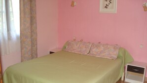 Une chambre à coucher avec un grand lit, une table de chevet, une commode, un rideau à motifs floraux et un tableau encadré accroché au mur.