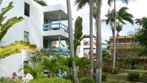 A resort with a white building featuring balconies, surrounded by lush greenery and palm trees. - Negril Beach Condo - Jamaica - Hotel Room, no/kitchen Unit 1 (Negril)