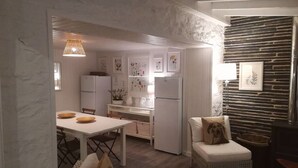 A compact kitchen with white cabinets, a dining table, and a seating area with a wicker chair. - Quinta dos Morangueiros, Douro Valley (Armamar)