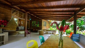 A wooden interior with a dining area, colorful chairs, and a table with a vase of flowers. - Casa Cerise (Cahuita)