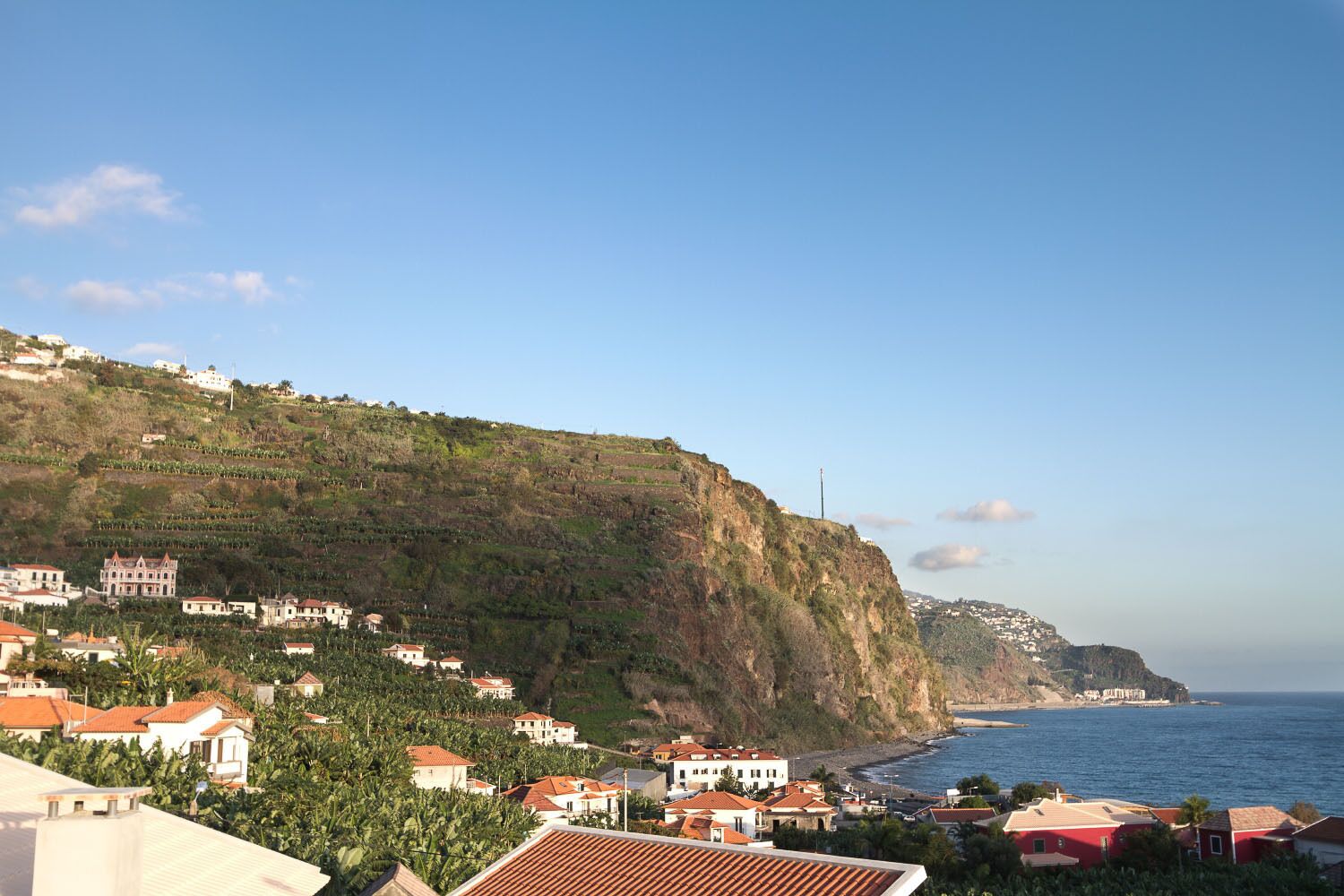 A coastal town with terraced houses on a hillside, a beach, and a clear sky.